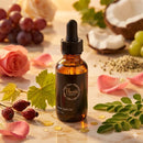 Bottle of Flourea Rose Gold Oil with natural ingredients like grapes, roses, and leaves on a light background
